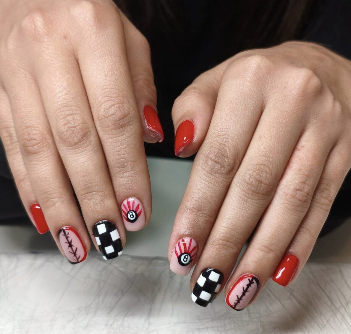 Red gel manicure with checkered, 8-ball and stitches nail art accents