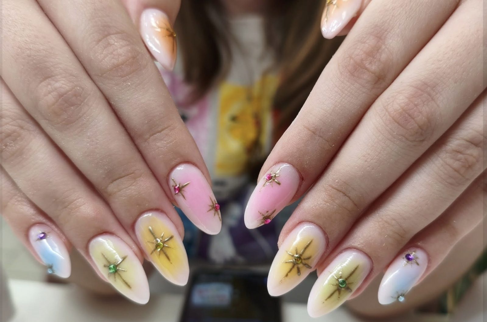 Pastel ombré almond gel manicure with hand-painted gold starburst nail art and multicolored rhinestone gems